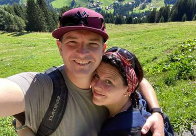 Ein Selfie eines jungen Paares vor einer sonnigen Berglandschaft